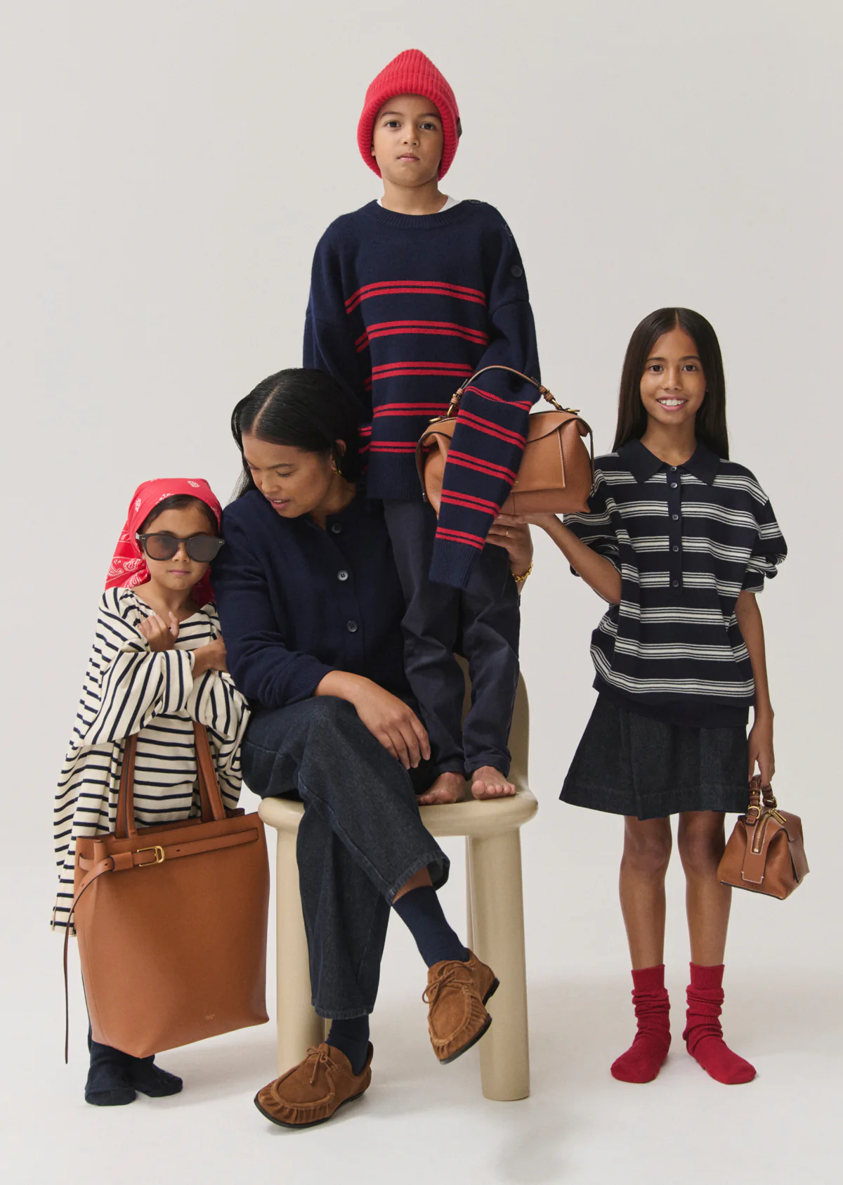 A mother sits on a stool with three children; one stands on the stool behind her, and two stand on either side of the stool.