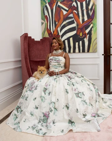 Elegant woman in a floral gown sits with a small dog in a grand interior, featuring a modern art painting and ornate details.
