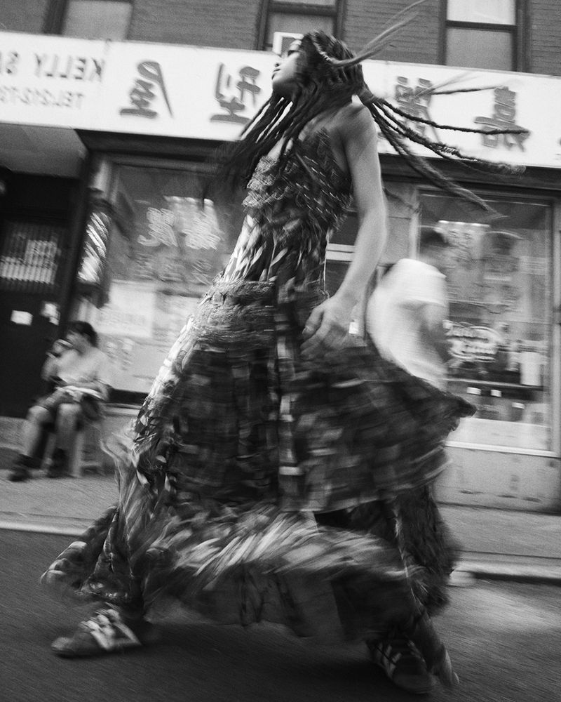 Woman with dreadlocks in flowing dress walks in street in black and white photo with blurred motion effect, capturing the essence of movement.