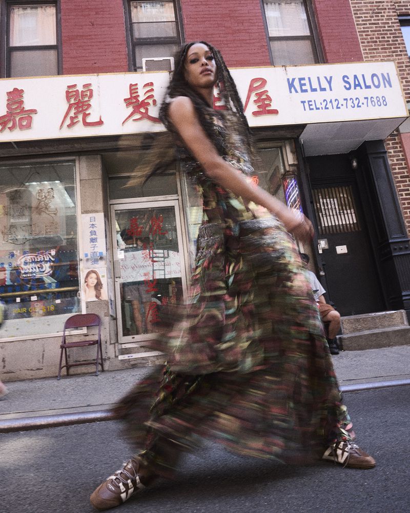 Woman in patterned dress walks on city street in front of Kelly Salon, capturing blurred motion in an outdoor urban fashion shot.