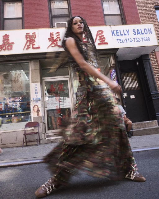 Woman in patterned dress walks on city street in front of Kelly Salon, capturing blurred motion in an outdoor urban fashion shot.