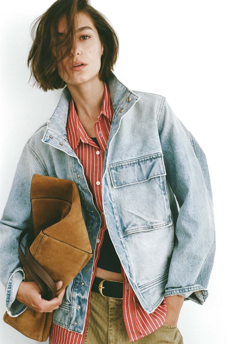 A woman with short brown hair poses in front of a white background, wearing a red and white striped shirt and denim jacket.