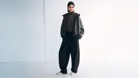 Model Alyosi S wearing a dark layered jacket and voluminous wide-leg trousers against a white studio background.