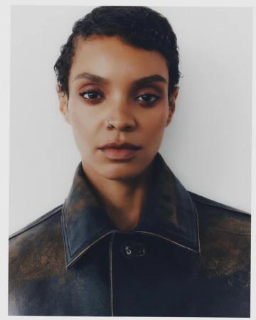 Close-up portrait of model Akira Reid wearing a distressed dark leather jacket against a plain off-white studio backdrop.