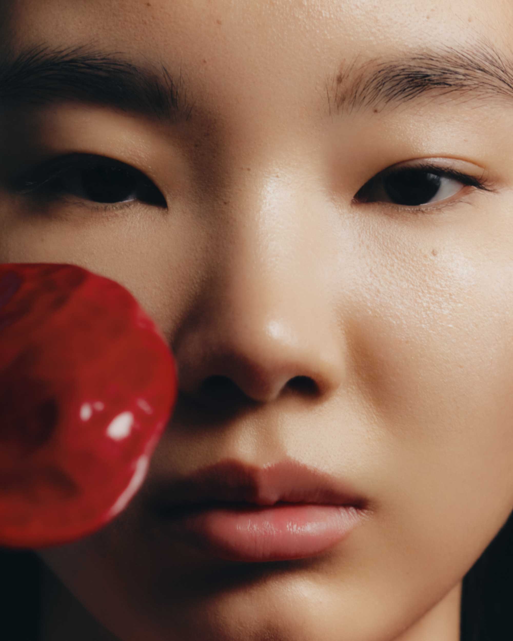 Close-up portrait of an Asian female model showcasing red lipstick and makeup in a beauty and fashion context against a dark backdrop.