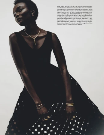 Elegant black woman poses in black V-neck dress with open crochet-style skirt, adorned with gold earrings, necklace, bangles, and rings.