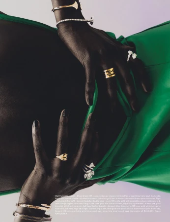 Dark-toned hands wearing gold and diamond rings and bracelets posed against a vibrant green dress.
