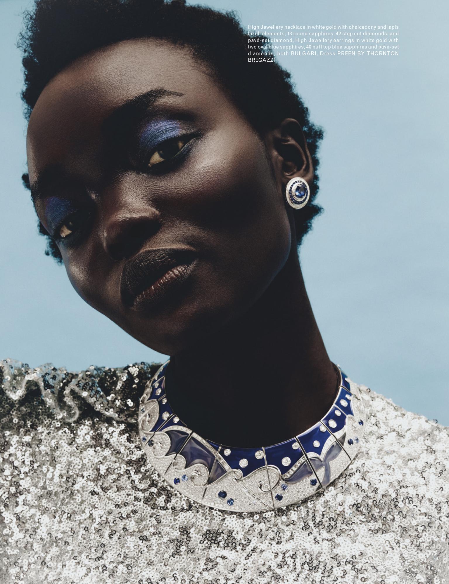 Close-up fashion shot of a dark-skinned woman with blue eye shadow, silver sequin dress, and a decorative blue and silver choker necklace.