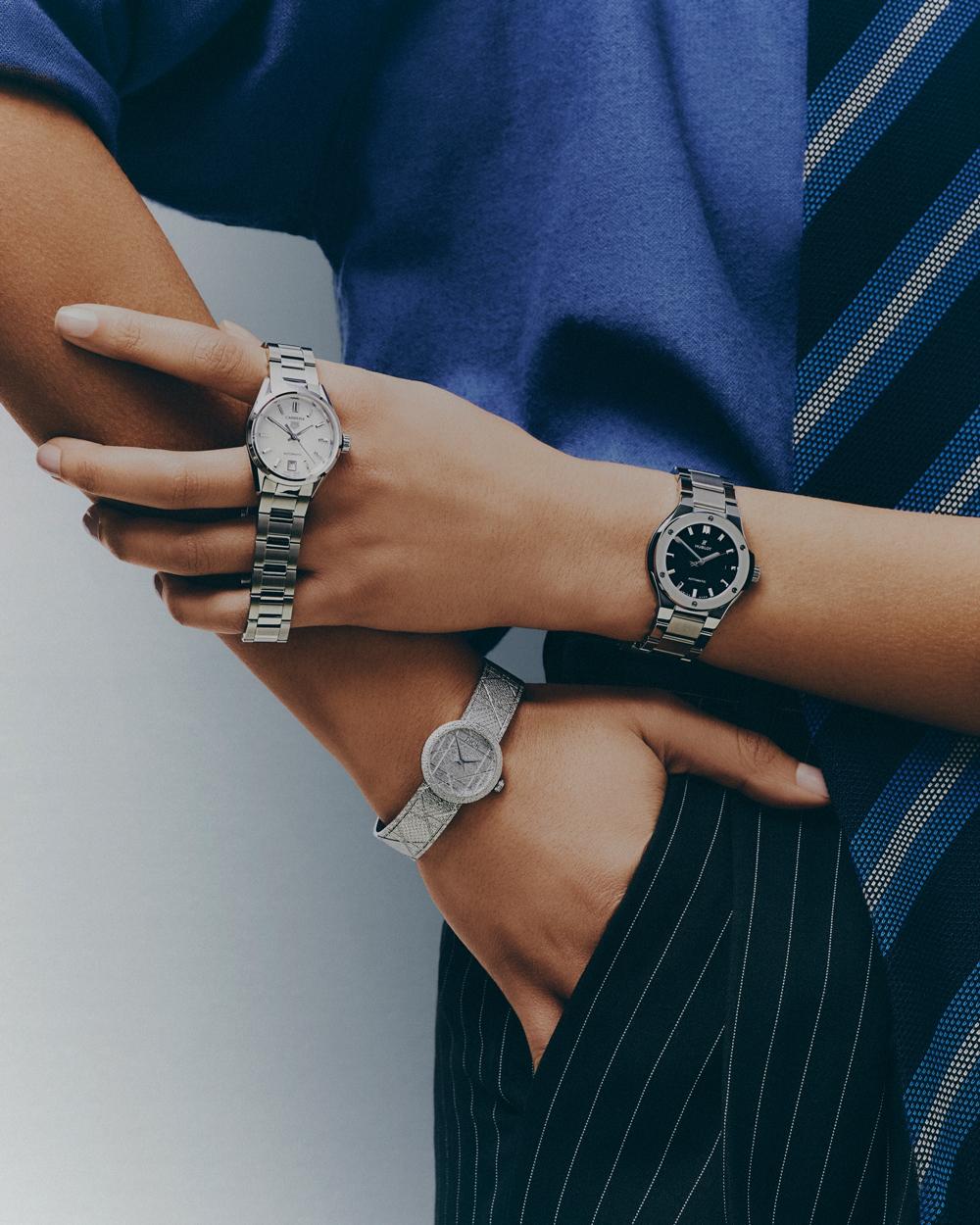 Close-up studio shot of three wristwatches on the arms of a person wearing a blue top and pinstripe pants. Fashion and accessorizing.