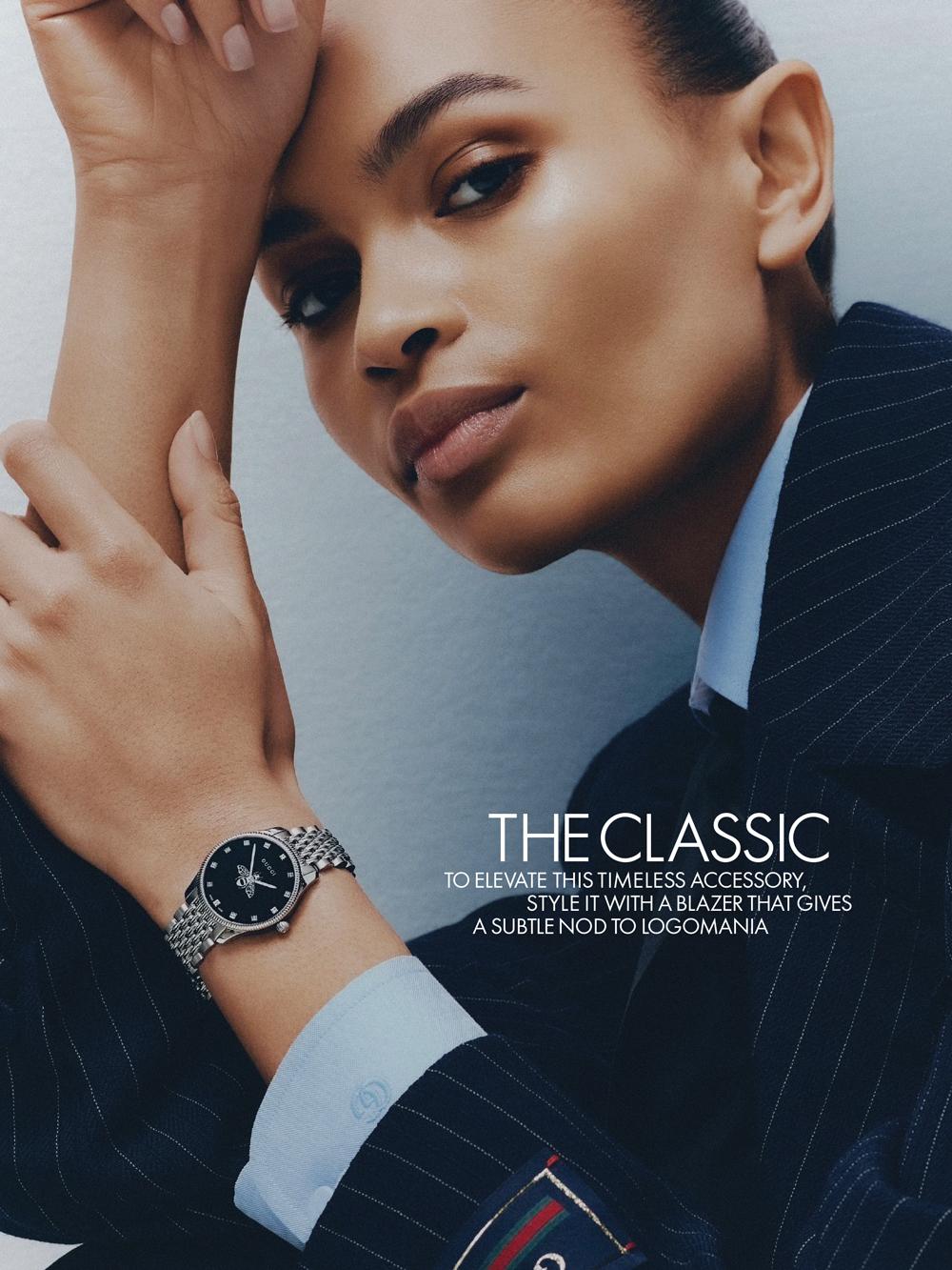 Elegant studio shot of a woman modeling a silver wristwatch with a dark dial, complemented by a pinstripe blazer and a light blue shirt.