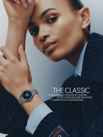 Elegant studio shot of a woman modeling a silver wristwatch with a dark dial, complemented by a pinstripe blazer and a light blue shirt.