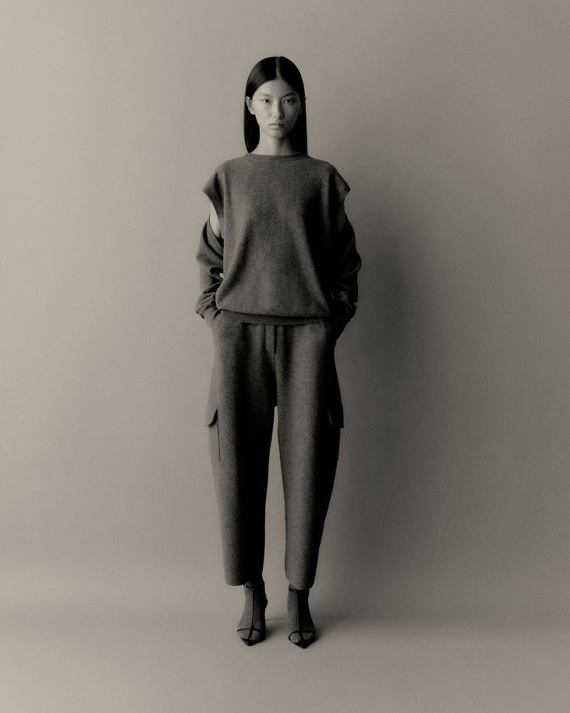 Monochrome full shot of an Asian woman in a relaxed sweater and wide-leg pants, standing in a neutral studio setting with an elegant pose.
