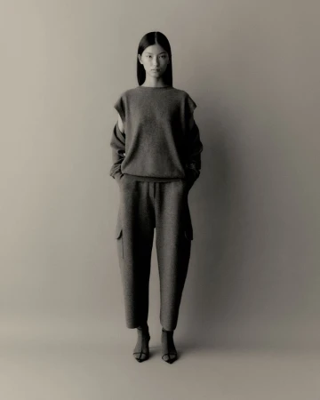Monochrome full shot of an Asian woman in a relaxed sweater and wide-leg pants, standing in a neutral studio setting with an elegant pose.