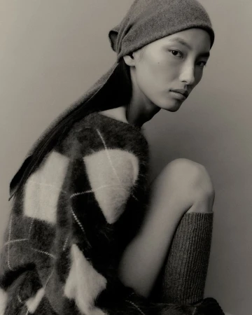 Monochromatic portrait of a model wearing a knit headscarf and oversized plaid sweater in a photo studio setting. Fashion editorial.