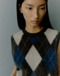 Close-up portrait of a model wearing an argyle knit vest against a plain grey studio background