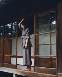 Model Rila Fukushima standing barefoot on wooden porch wearing grey jacket and skirt for Cordera FW25 campaign