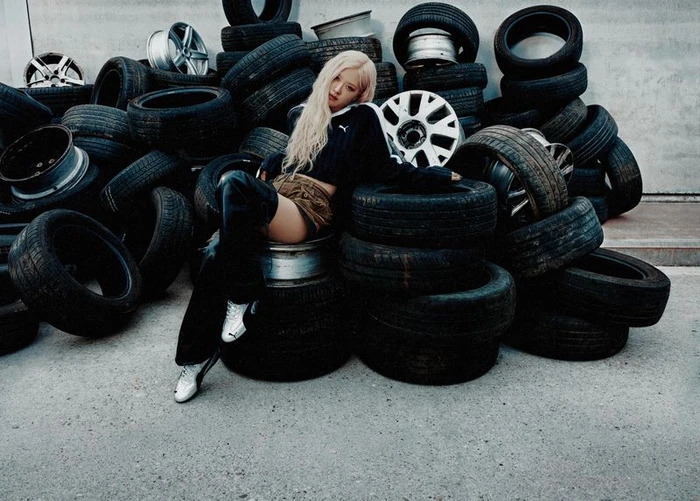 Rosé seated amidst a large stack of discarded car tires wearing a Puma crop top and boots.