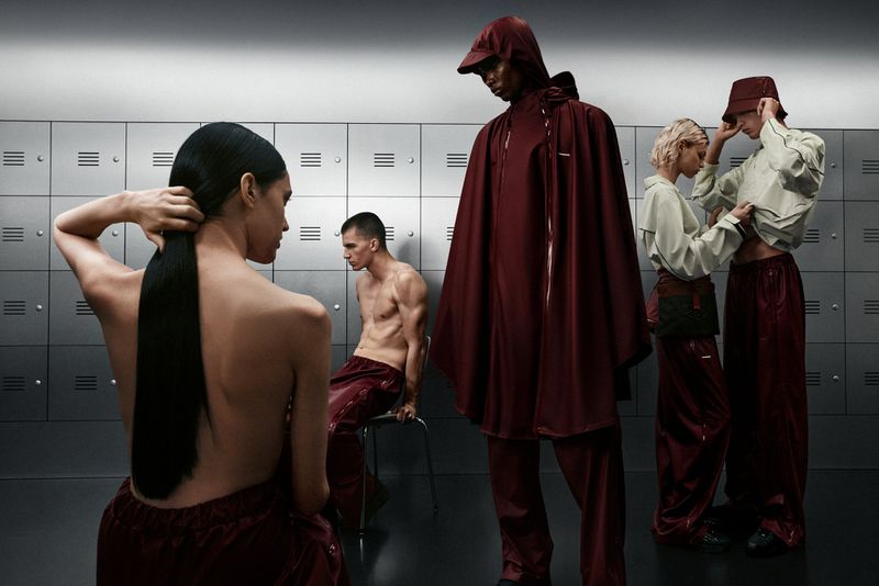 Fashion shot in a locker room with 5 models of diverse ethnicities, featuring modern clothing, including a hooded cape, against metal lockers.