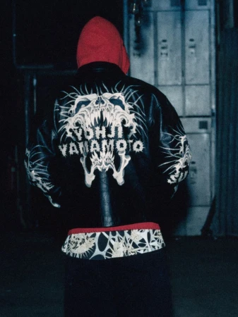 Back view of a person wearing a black leather jacket with white skull and bone designs, paired with a red hoodie indoors.
