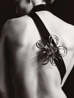 Monochrome portrait of a model from behind wearing a black strap with a sculpted flower ornament