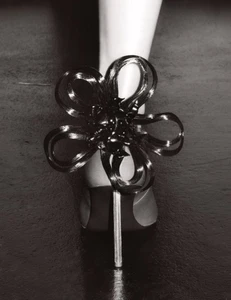 Close-up of a high-heeled shoe adorned with a sculptural black hair ornament wrapping around the ankle.