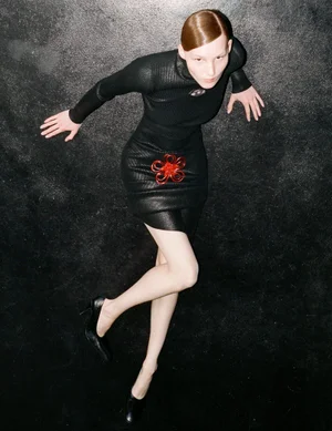 Model in a black fitted top and skirt with a red flower detail posing against a dark textured background
