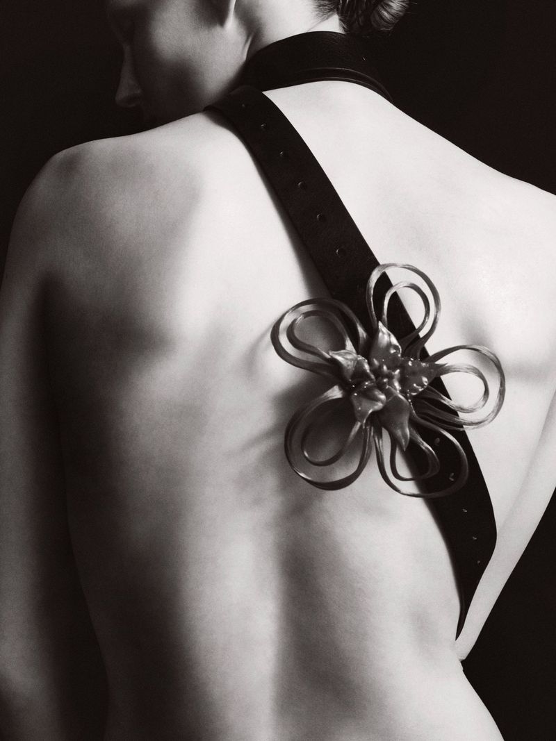 Monochrome studio shot of woman's back adorned with a dark strap and floral design, against a dark background.