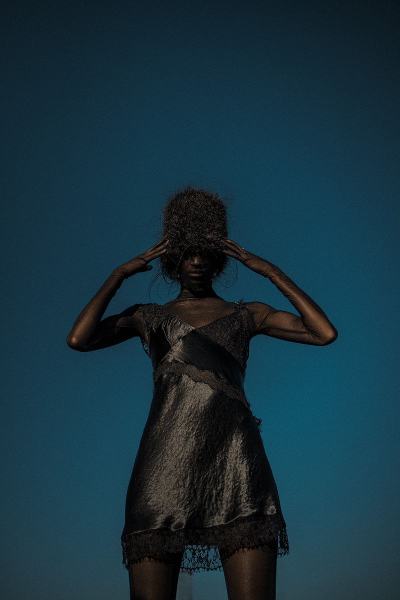 Model wearing a black lace slip dress posing against a deep blue sky for Collina Strada SS26.