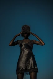 Model wearing a black lace slip dress posing against a deep blue sky for Collina Strada SS26.
