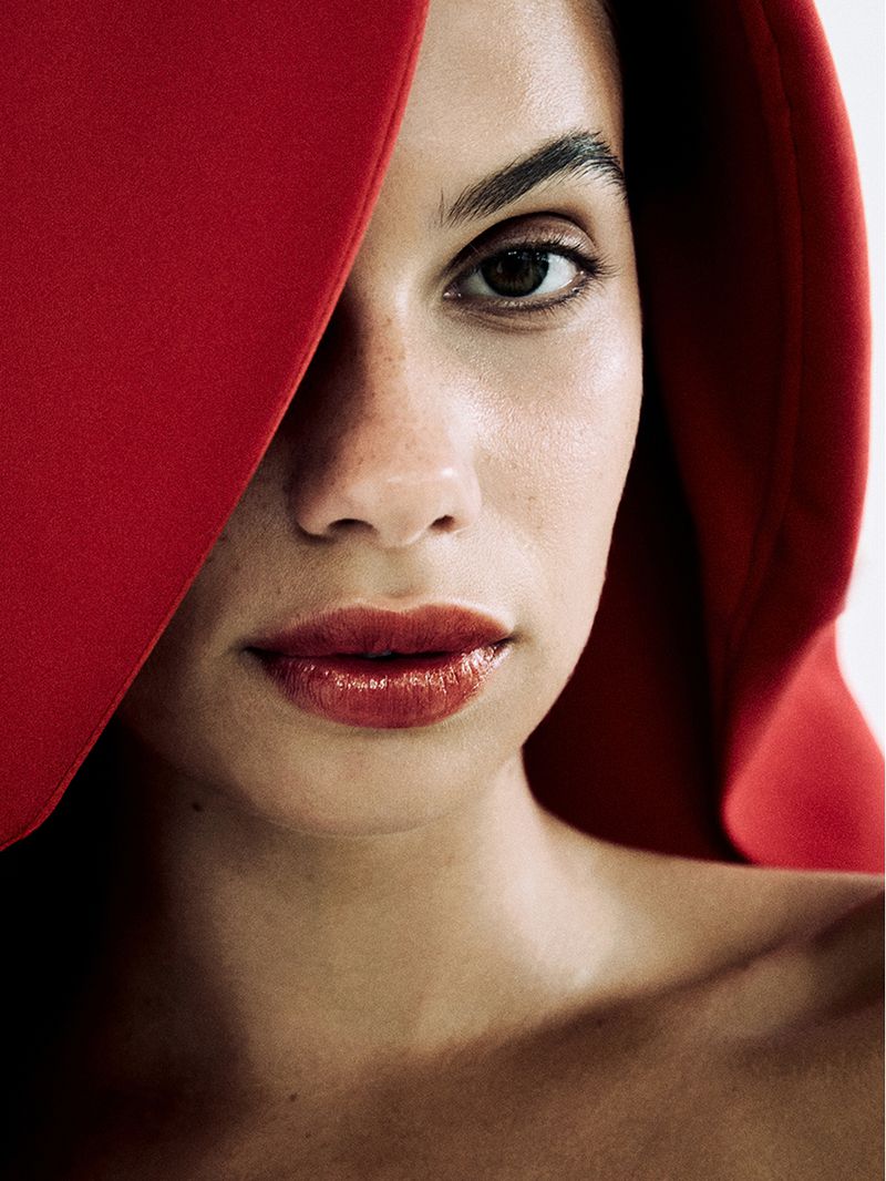 Close-up portrait of a woman with glossy red lips, partially covered by a draped red textile, creating a striking and dramatic effect.