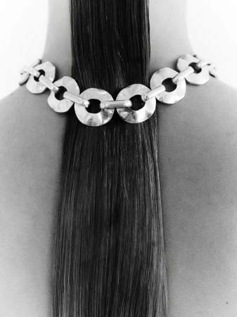 Close-up of a woman's back featuring a metal ring necklace draped over her bare shoulders, highlighting the contrast with her straight dark hair.
