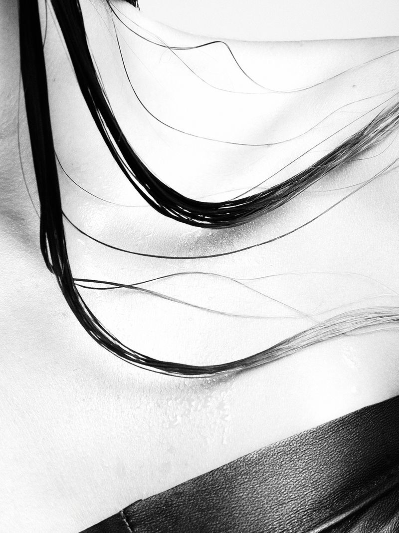 Close-up black and white shot of the upper chest and neck of an adult female with wet, dark hair, and a black leather-like collar.