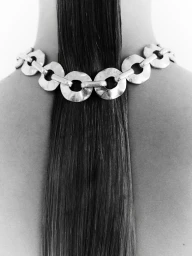 Close-up rear view of a person wearing a thick silver chain necklace over a long straight dark ponytail.