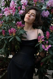 Woman in a black dress posing amongst pink rhododendron flowers for The Walk project in Contributor Magazine