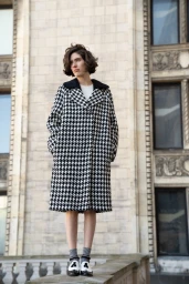 Model standing outdoors wearing a black and white houndstooth coat against an ornate stone building exterior.