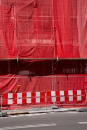 Red mesh scaffolding net and red and white striped construction barriers along an asphalt street.