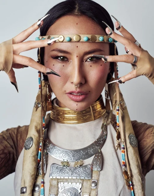 Portrait of an adult woman with long dark hair and tribal-style jewelry posing in front of a solid white background in a photo studio.