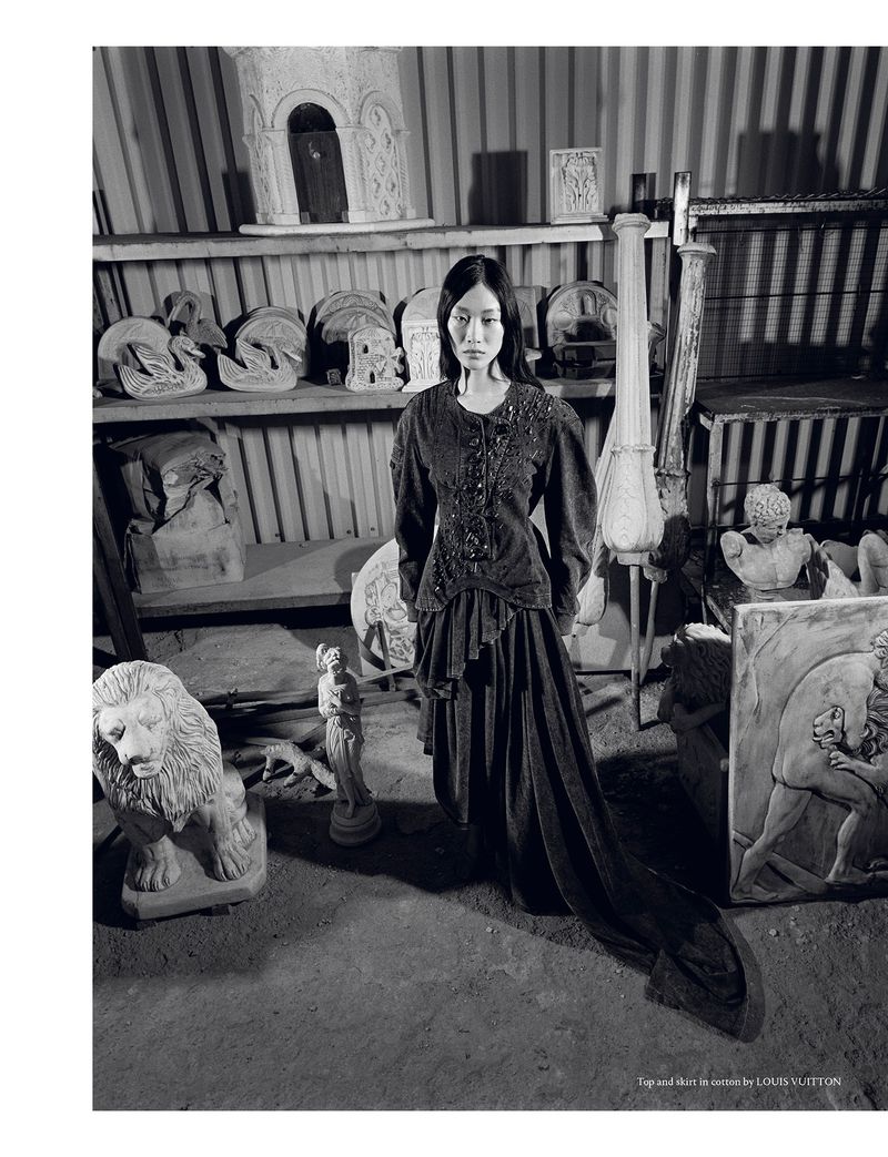 Monochrome shot of a woman in a vintage-style dress, surrounded by classical sculptures in an indoor setting, providing a timeless aesthetic.