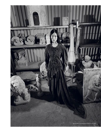 Monochrome shot of a woman in a vintage-style dress, surrounded by classical sculptures in an indoor setting, providing a timeless aesthetic.