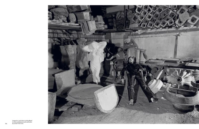 A young woman in leather attire poses among discarded concrete forms in a weathered indoor industrial setting, captured in black and white.