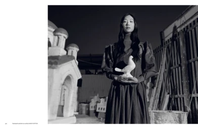 Model Sora Choi in a dark pleated Louis Vuitton dress holding a white bird sculpture in a monochrome outdoor editorial.