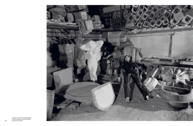 Model Sora Choi in dark clothing reclining in a cluttered industrial studio filled with statues and molds, photographed by Yorgos Lanthimos.