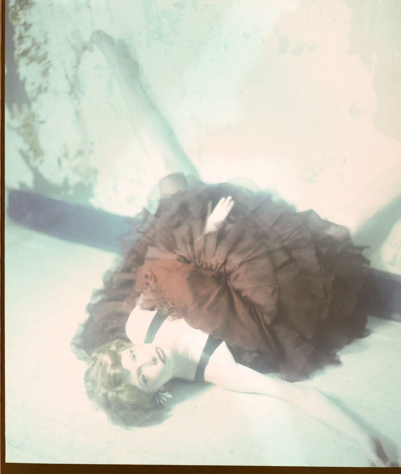 Model Edwina Preston reclining on the floor wearing a voluminous brown ruffled tulle skirt and black top.