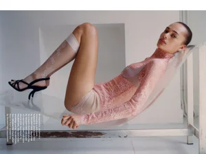 Model Annemary Aderibigbe reclining in a sheer pink lace bodysuit, ribbed knit shorts, and lace stockings on a sling lounger.