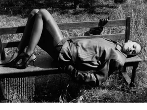 Model Annemary Aderibigbe lies back across a wooden bench outdoors wearing a leather jacket and heels in black and white.
