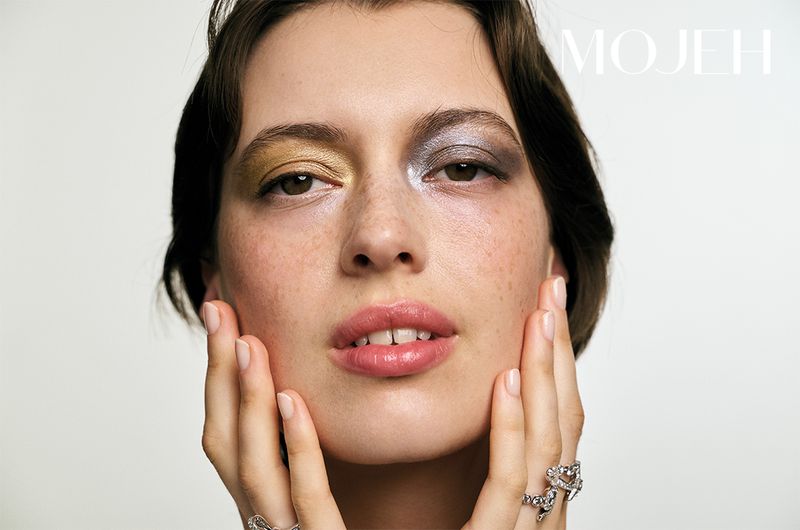 Close-up shot of a model showcasing dual-toned eye makeup, with gold on one eyelid and silver-grey on the other, set against a plain backdrop.