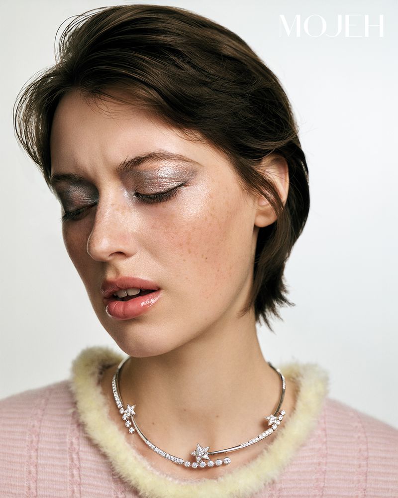 Model Iris Delcourt wearing a diamond star collar necklace and a pink knit sweater against a white backdrop for Mojeh Magazine.