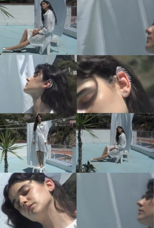 A young woman with long dark hair models an ear cuff and wears a white dress in a series of outdoor rooftop shots.