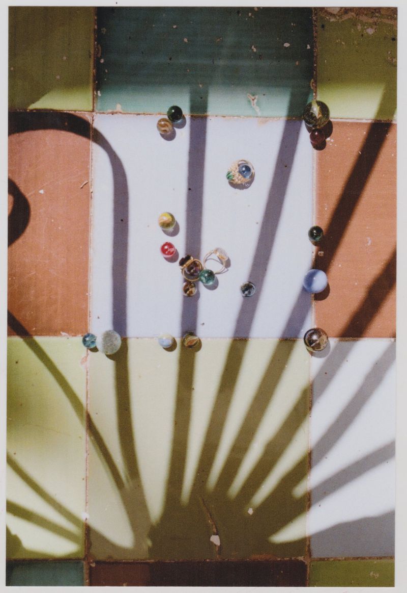 Overhead shot of colorful glass marbles scattered on a tiled surface with strong geometric shadows creating a sense of depth.
