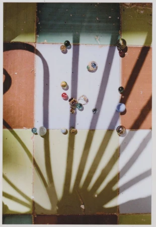 Overhead shot of colorful glass marbles scattered on a tiled surface with strong geometric shadows creating a sense of depth.